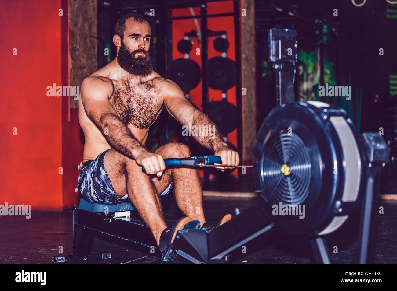 Bearded young man using rowing machine in the gym Stock Photo
