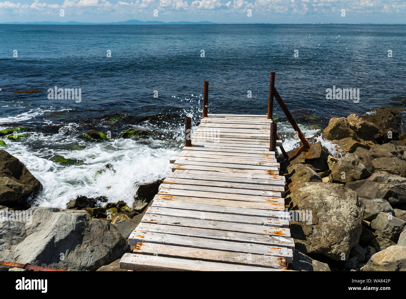 An old, wooden jetty over the beautiful Black Sea in Bulgaria, standing on a stony shore, in the background a sky with clouds. Stock Photo