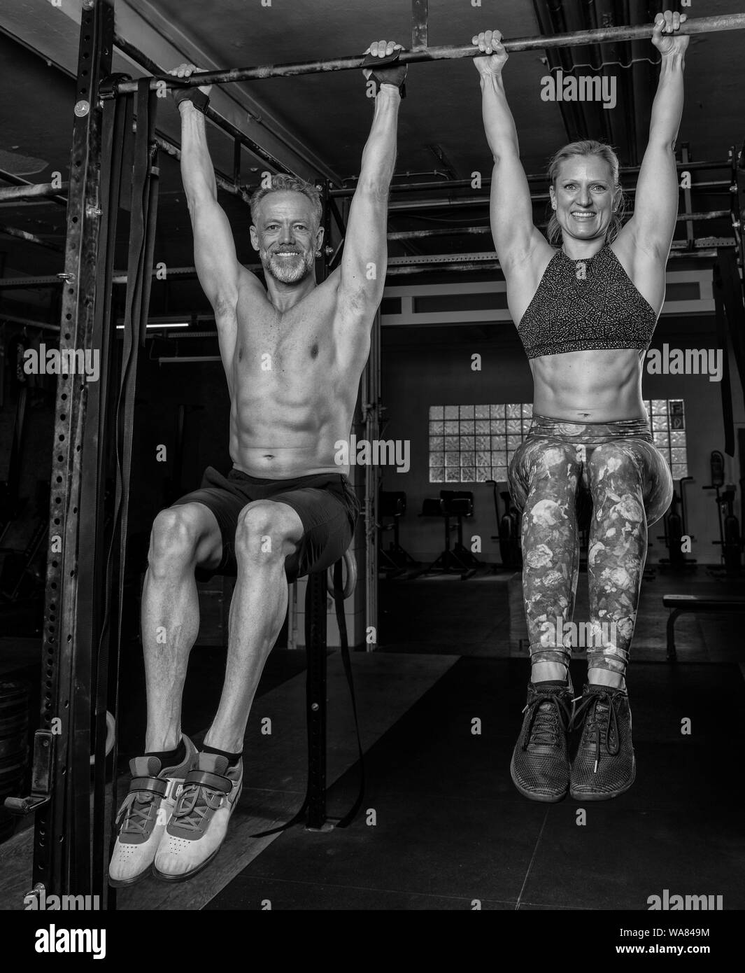 A handsome middle aged couple is doing a fitness training together and having fun. Muscular older man and woman are hanging on the horizontal bar. Stock Photo