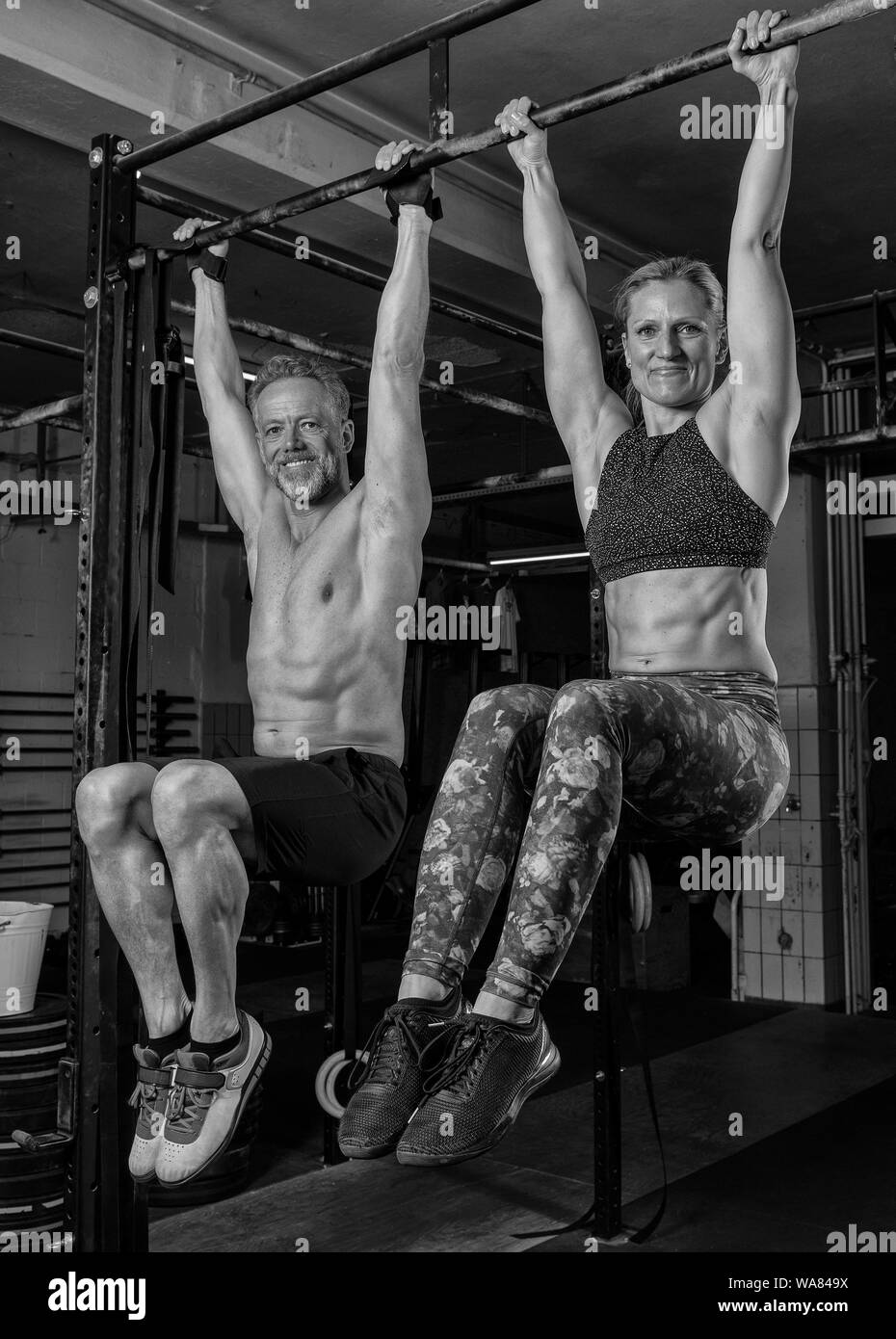 A beautiful middle aged couple is doing a fitness training together and having fun. Muscular older man and woman are hanging on the horizontal bar. Stock Photo