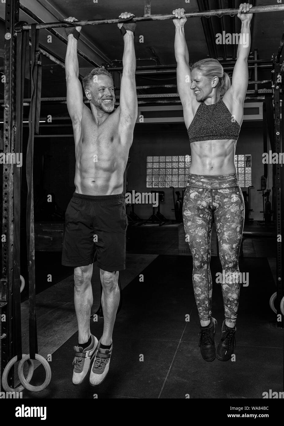 An attractive middle aged couple is doing a fitness training together and having fun. Strong older man and woman are hanging on the horizontal bar. Stock Photo