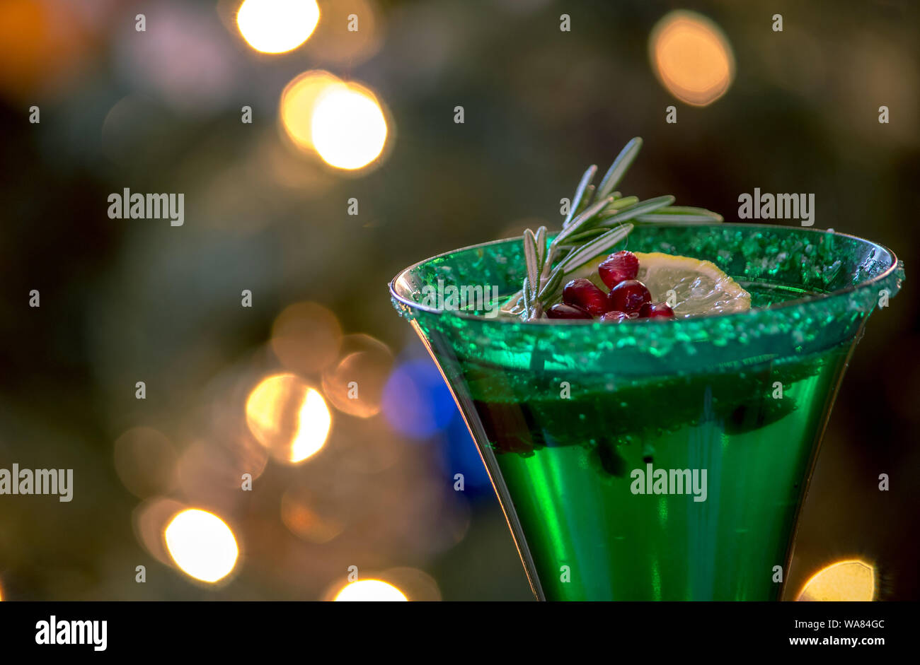 Green champagne flute with rosemary, pomegranate seeds and a sprig of lime floating on the bubbly Stock Photo