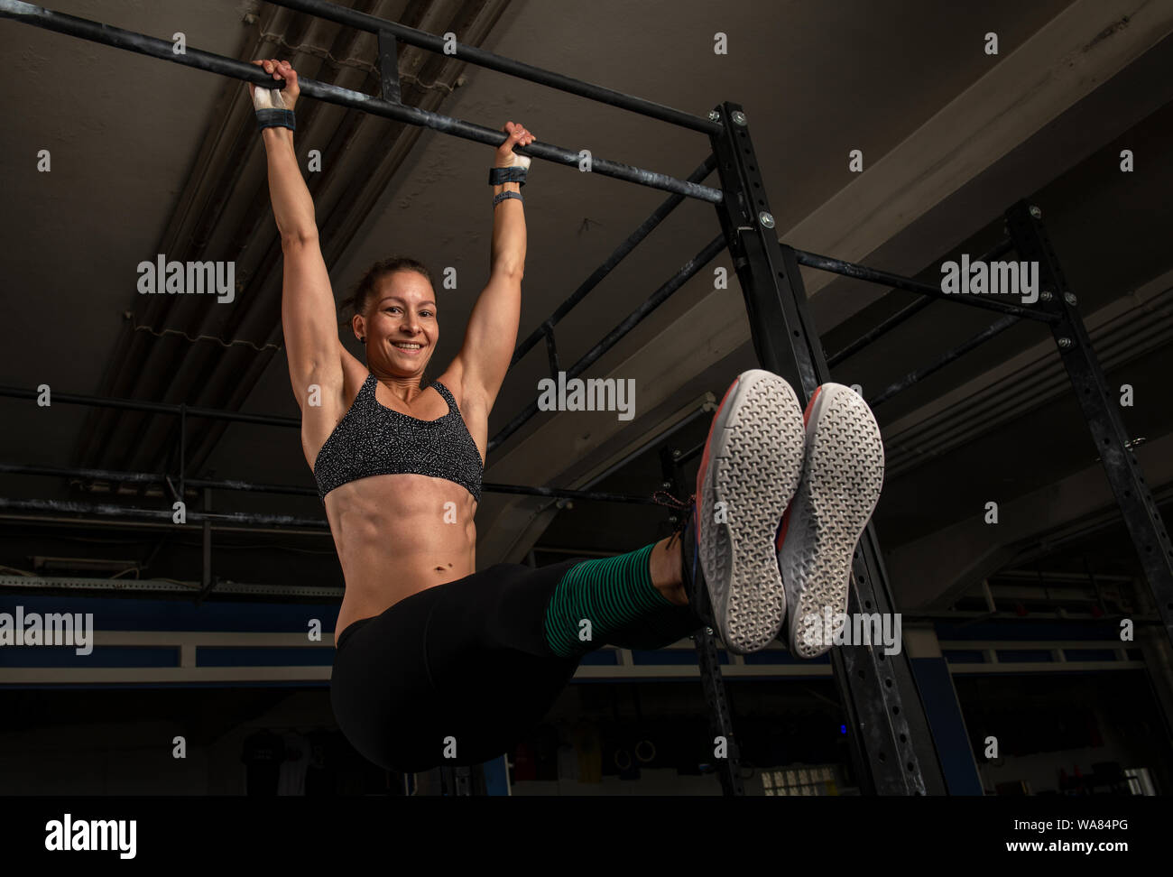 A sporty woman is doing a fitness workout and having fun.The muscular and attractive woman is doing the exercise l sit on the horizontal bar. Stock Photo