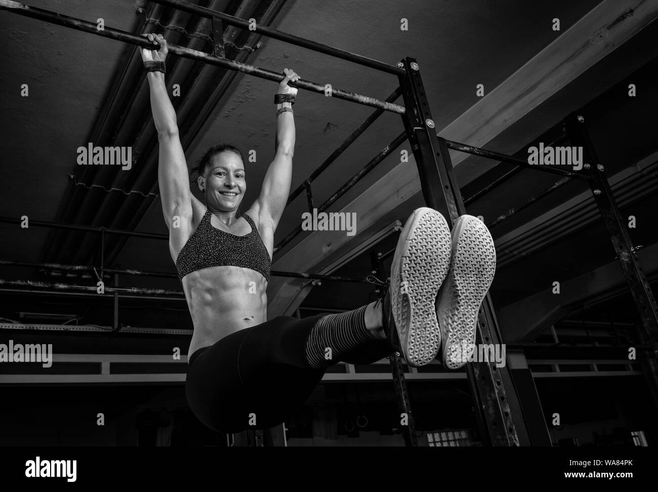 An athletic woman is doing a fitness workout and having fun.The muscular and attractive woman is doing the exercise l sit on the horizontal bar. Stock Photo