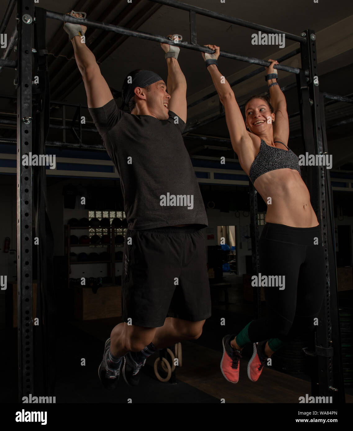 An athletic couple is doing a fitness workout together and having fun.The muscular and attractive man and woman are doing the exercise toes to bar.v Stock Photo