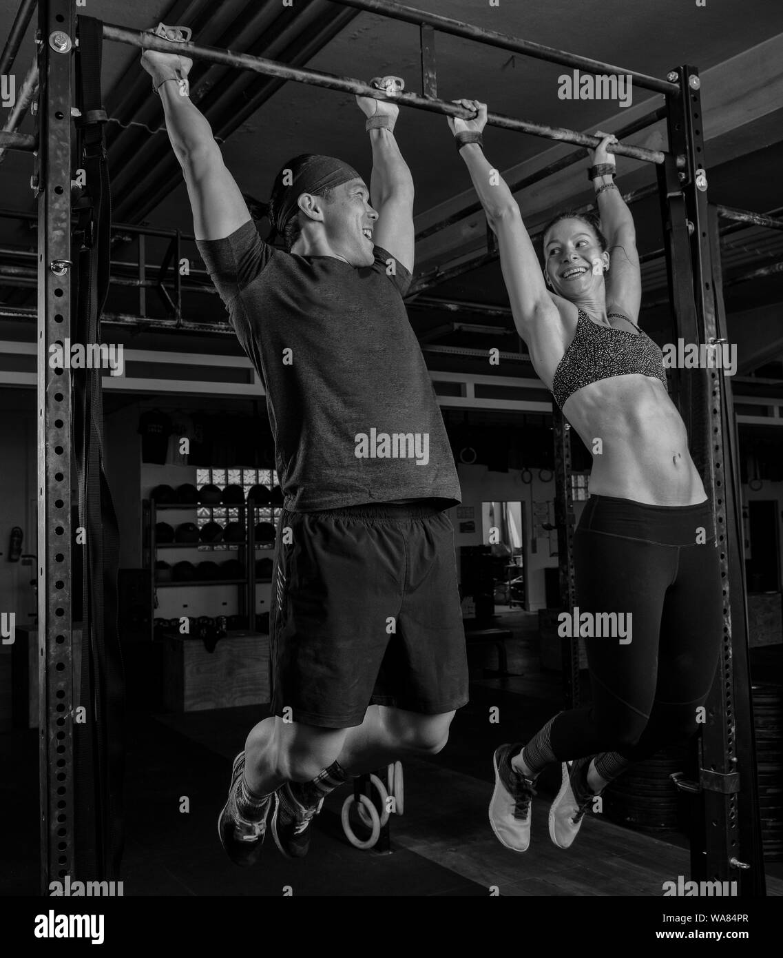 An athletic couple is doing a fitness workout together and having fun.The muscular and attractive man and woman are doing the exercise toes to bar. Stock Photo