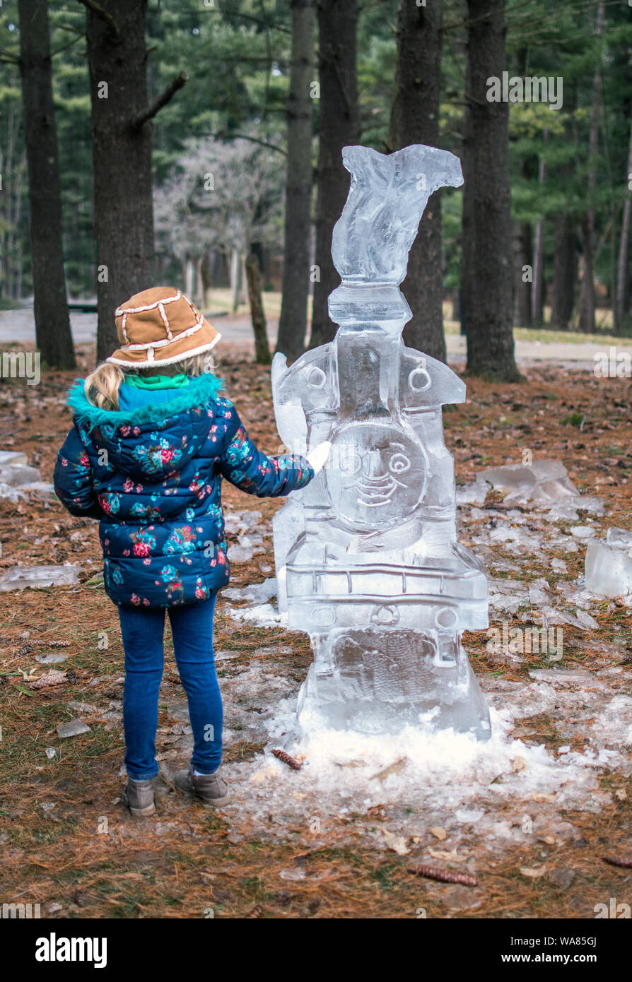 March 17, 2019 Bendix woods Indiana USA; a title girl examines an ice carving of Thomas the tank train engine, at the sugar camp days event in Indiana Stock Photo