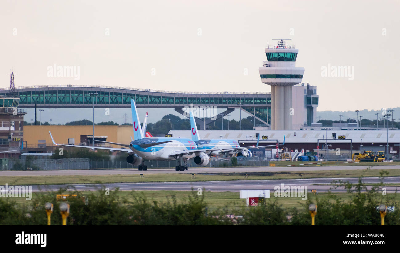 A Tui Airways Boeing 757-200 plane turns off the runway in front of the air traffic control tower and the Gatwick Pier 6 Bridge Stock Photo