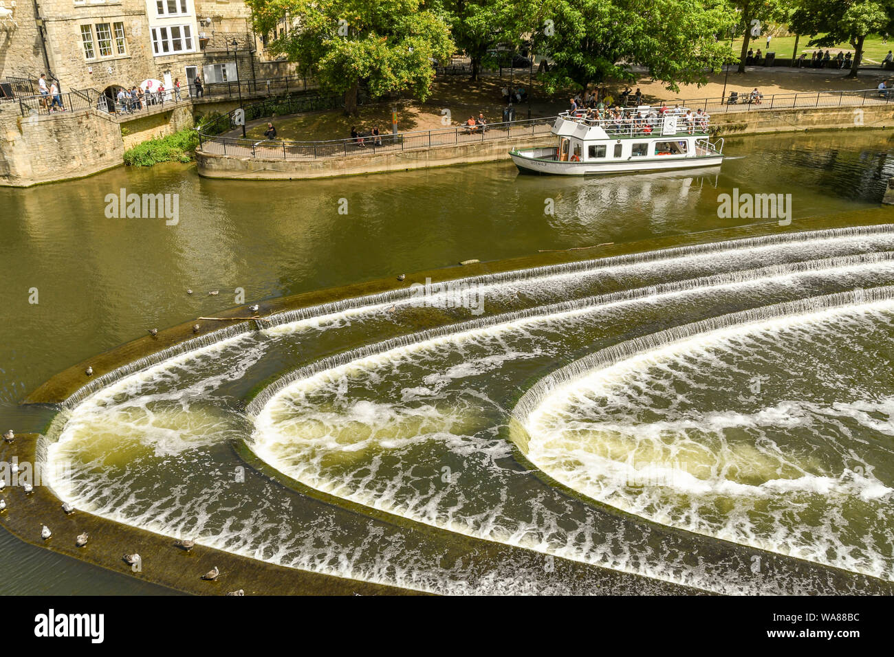BATH, ENGLAND - JULY 2019: The horseshoe shaped Pulteney Weir on the River Avon in the centre of Bath. A tourist boat is in the background. Stock Photo