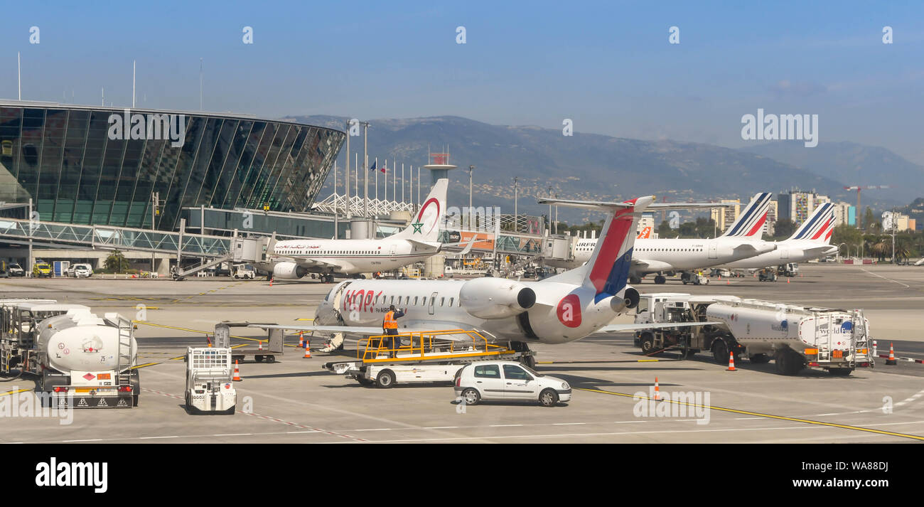 CANNES, FRANCE - APRIL 2019: Small commuter plane surrounded by ground handling equipment at Nice Airport. In the background is the terminal building Stock Photo