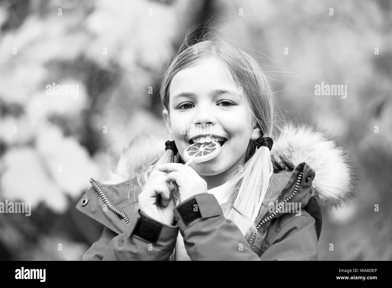 Happy little girl in autumn forest. Feeling protected at this autumn day. Small child with autumn leaves. Little girl eat lollipop. Autumn fashion. Happy childhood. Happy to be around. Enjoying fall. Stock Photo