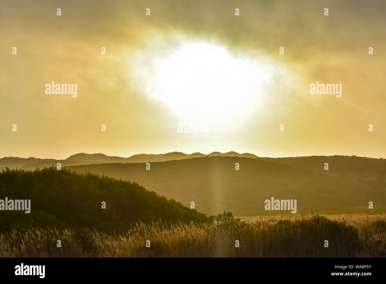 Sun breaking through clouds over hills at sunset. Stock Photo