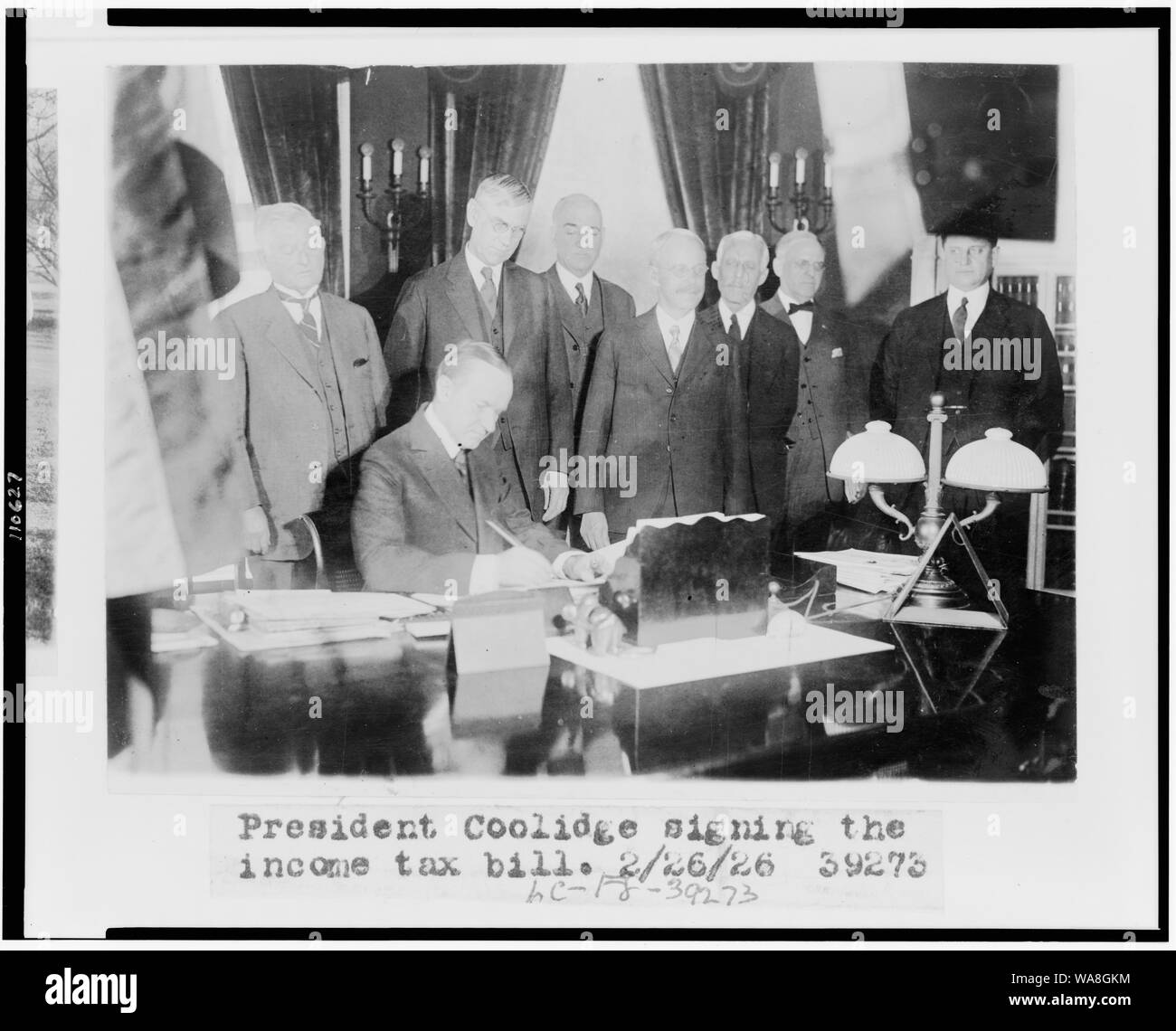 Calvin Coolidge signing the income tax bill, also known as the Mellon tax bill. Secretary of the Treasury Andrew Mellon is the third figure from the right, and Director of the Budget, General Herbert Mayhew Lord, is to Mellon's left Stock Photo