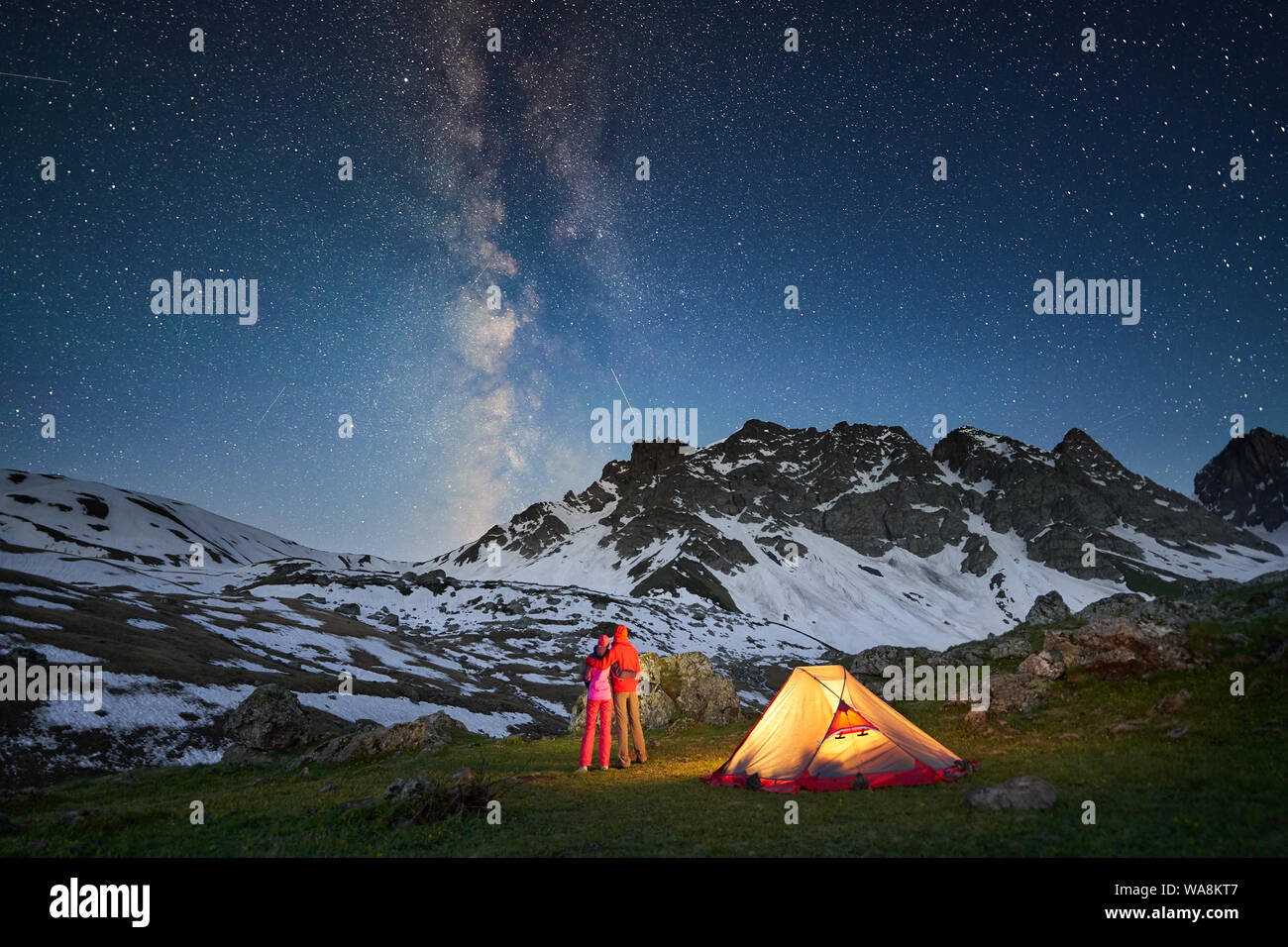 Couple standing near tent and looking at the milky way in mountains at night Stock Photo