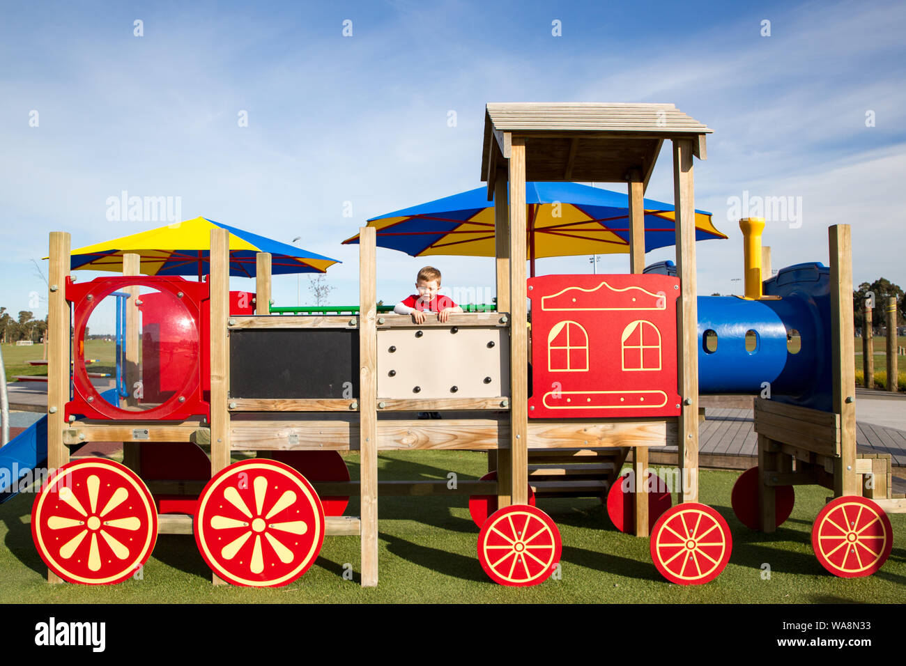 A young preschool child climbs up on the colorful wooden activity train at a public playground in New Zealand Stock Photo