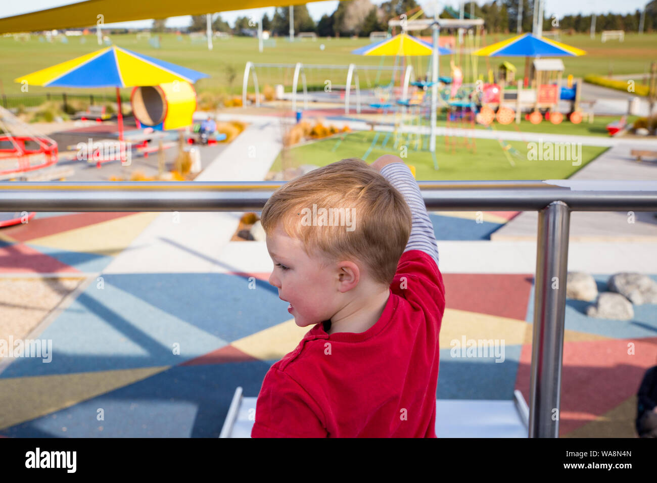 A young child waits at the top of the slide for his friend at Foster Park, Rolleston, New Zealand Stock Photo