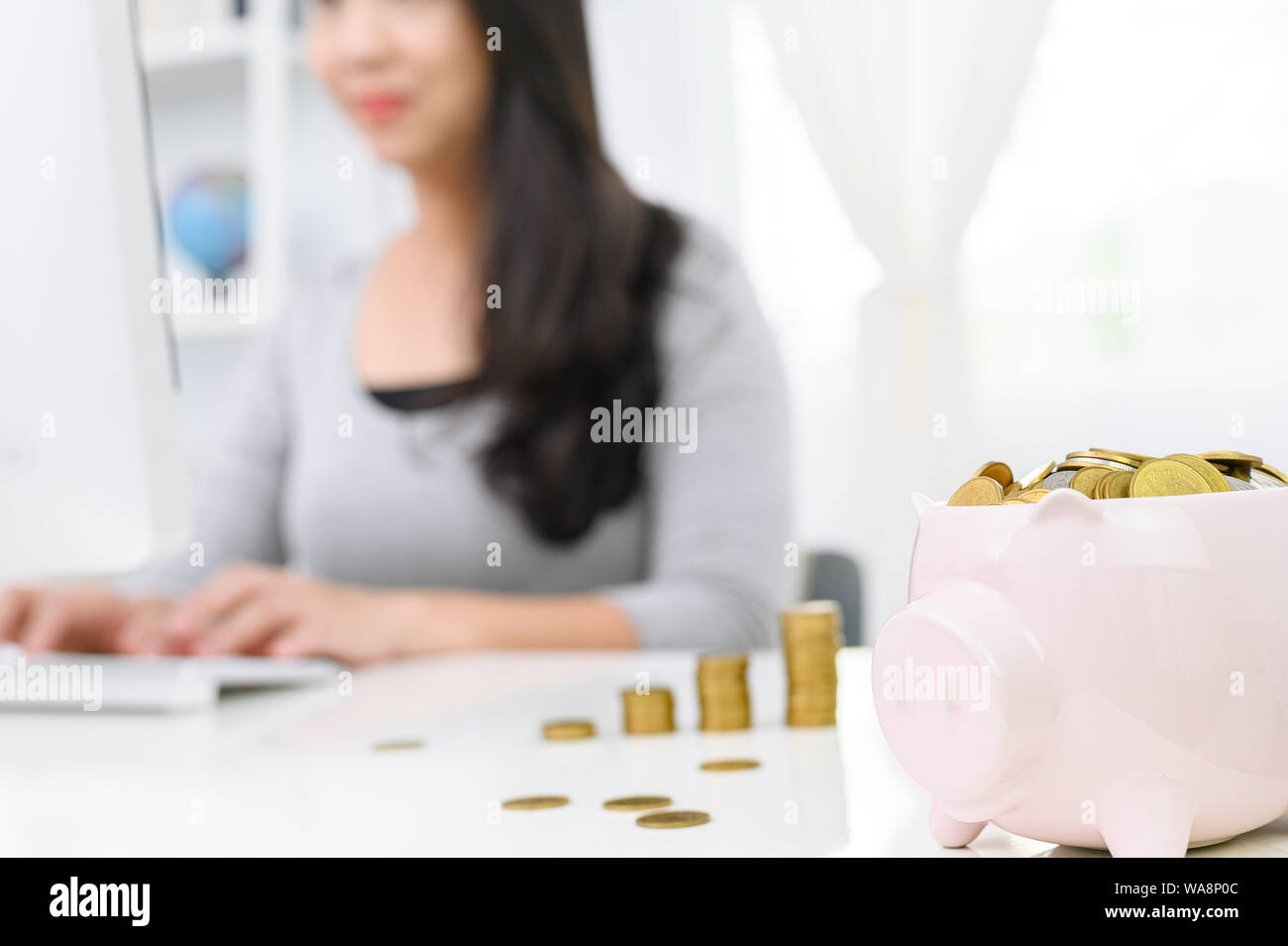 Cute piggy bank with gold coin and blur Woman working on computer at ...