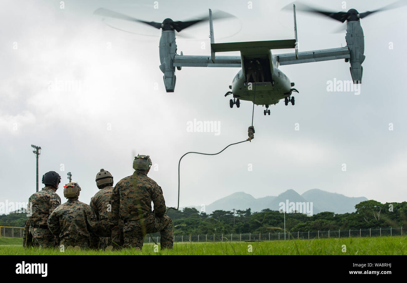 U.S. Marines watch as a fellow Marine fast ropes out of an MV-22 Osprey during helicopter rope suspension techniques training on Camp Hansen, Okinawa, Japan, Aug. 13, 2019. U.S. Marines with 3rd Reconnaissance Battalion and Soldiers with 1st Special Forces Group performed rappelling and fast rope operations as part of the HRST training, hosted by Expeditionary Operations Training Group, III Marine Expeditionary Force Information Group. The training is meant to provide the students with the ability to conduct helicopter insertions without landing the aircraft. (U.S. Marine Corps photo by Lance Stock Photo