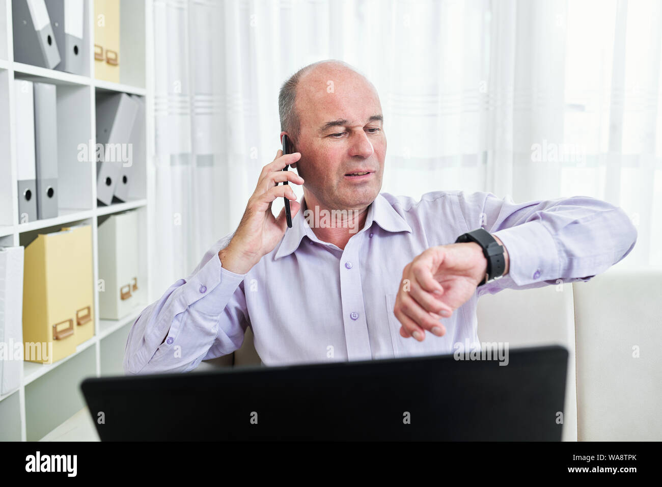 Middle-aged businessman sitting at office desk and checking time on his ...