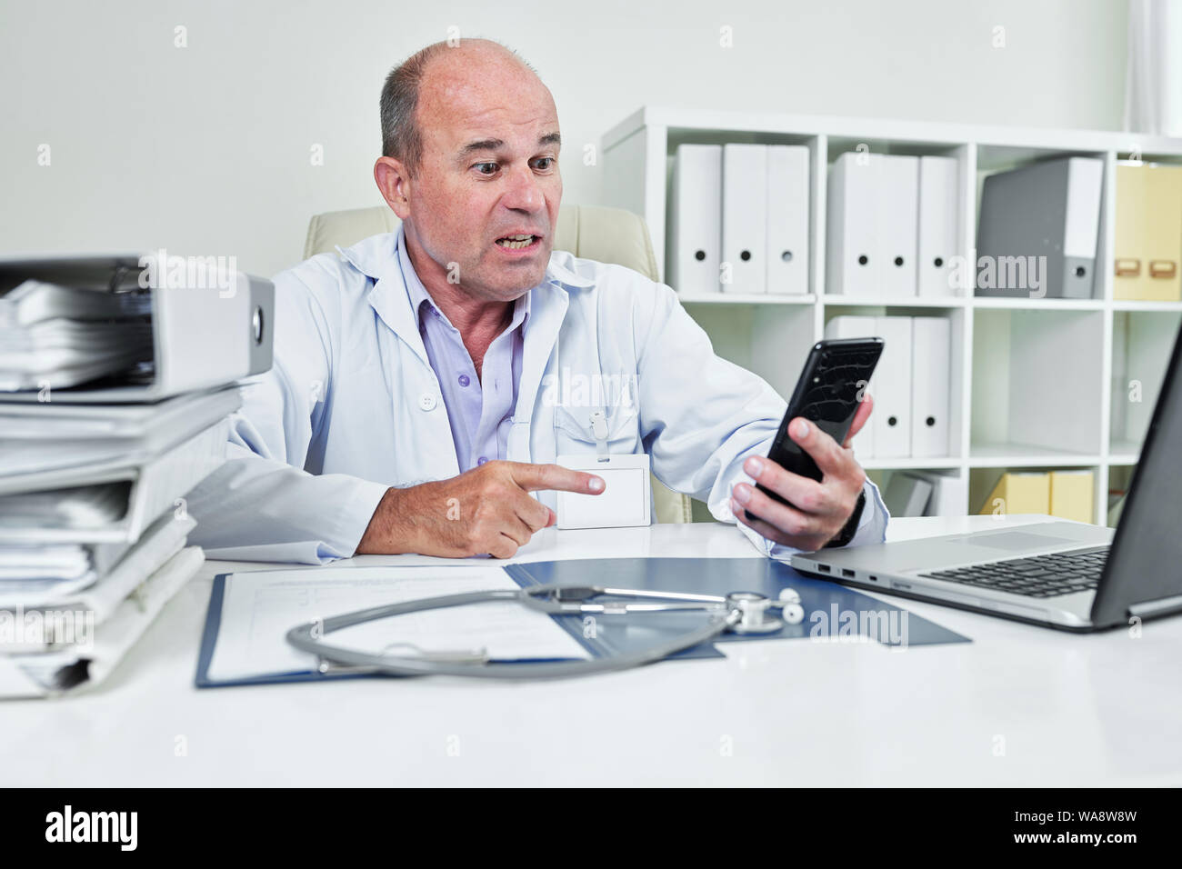 Angry emotional general practitioner in labcoat video calling coworker or annoying patient Stock Photo