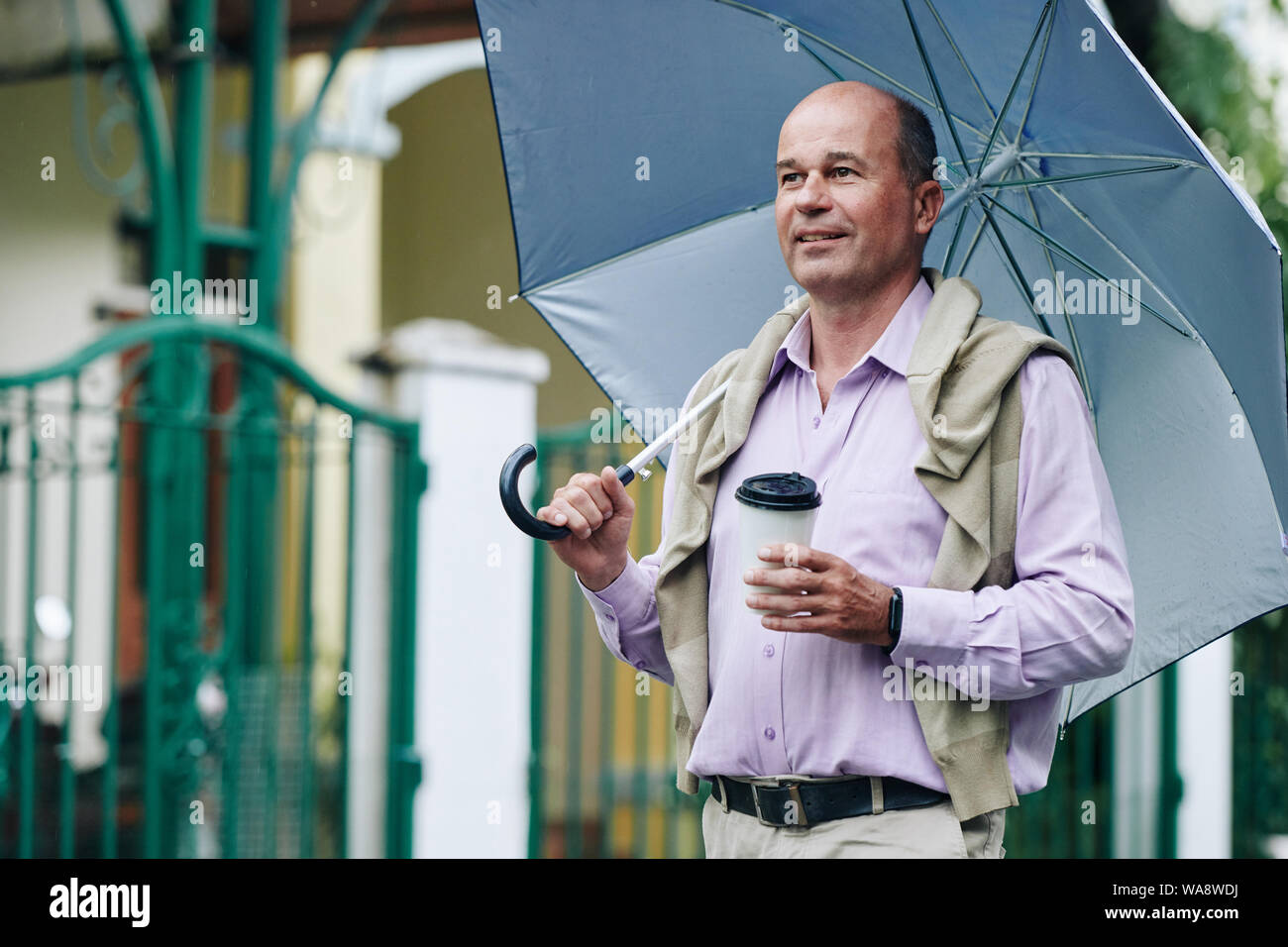 Elegant mature man walking outdoors with cup of take away coffee on rainy day Stock Photo