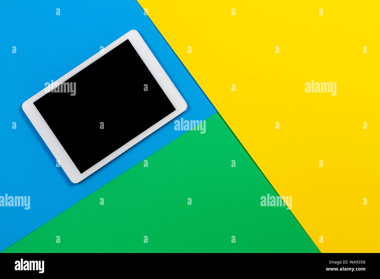 Digital tablet computer on light blue, green and yellow background. Top view Stock Photo