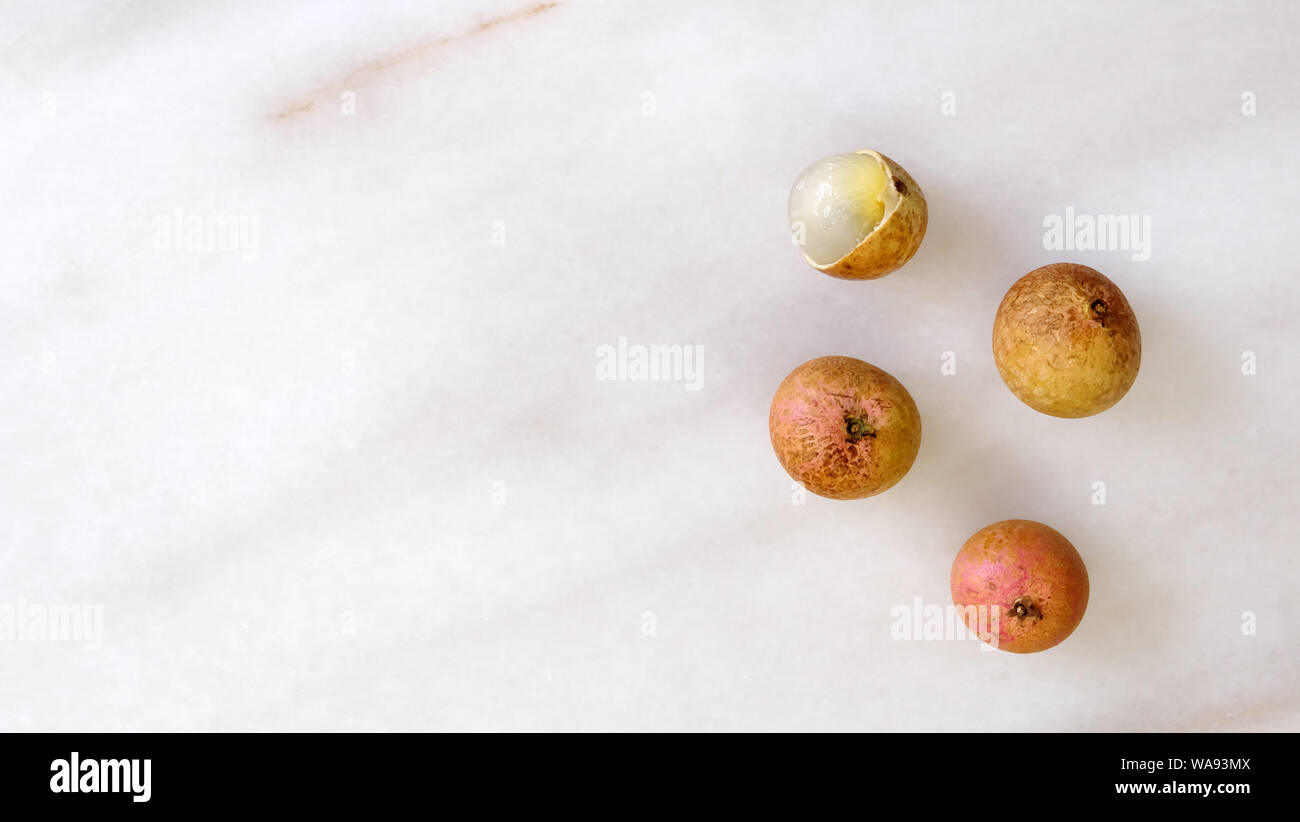Top view of longan fruits on a marble surface, with empty space on the left. Longan is an edible tropical fruit that is commonly found in traditional Stock Photo