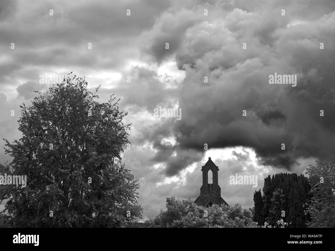 Black and White photo of a cloudy sky and a chapel tower at a cementary ...