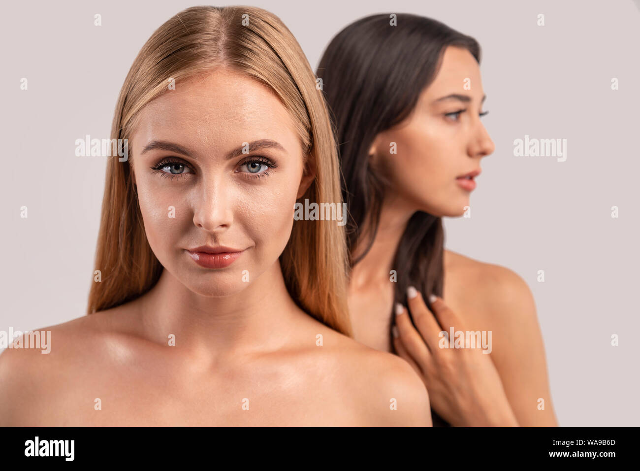 Slightly smiling blonde and thoughtful blurred brunette with naked shoulders isolated white background Stock Photo