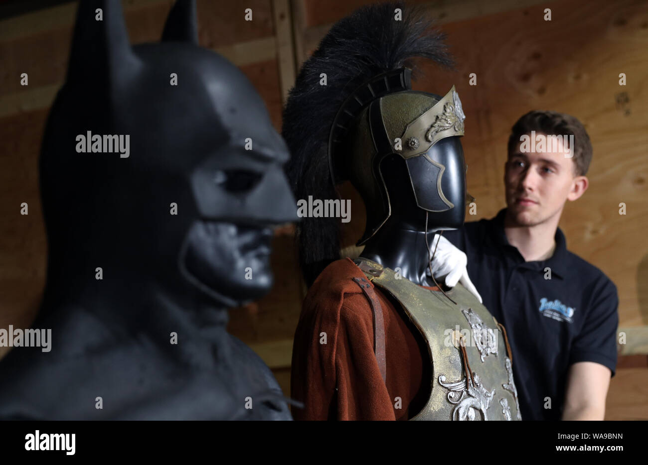 A Prop store employee adjusts the Maximus screen matched Roman general armour worn by Russell Crowe in the 2000 film Gladiator (estimate ??30-50,000), alongside Michael Keaton's Batsuit from the 1989 film Batman (estimate ??80-120,000), during a preview of the forthcoming film and television memorabilia auction at the Prop Store head office near Rickmansworth. Stock Photo