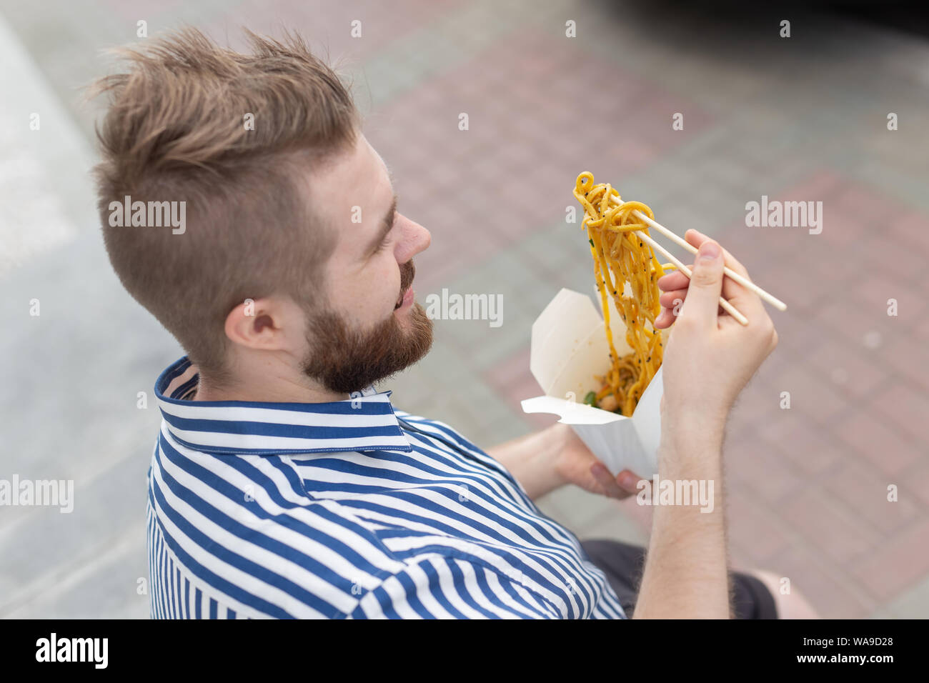 Young male hipster with a mustache and beard is eating chinese noodles