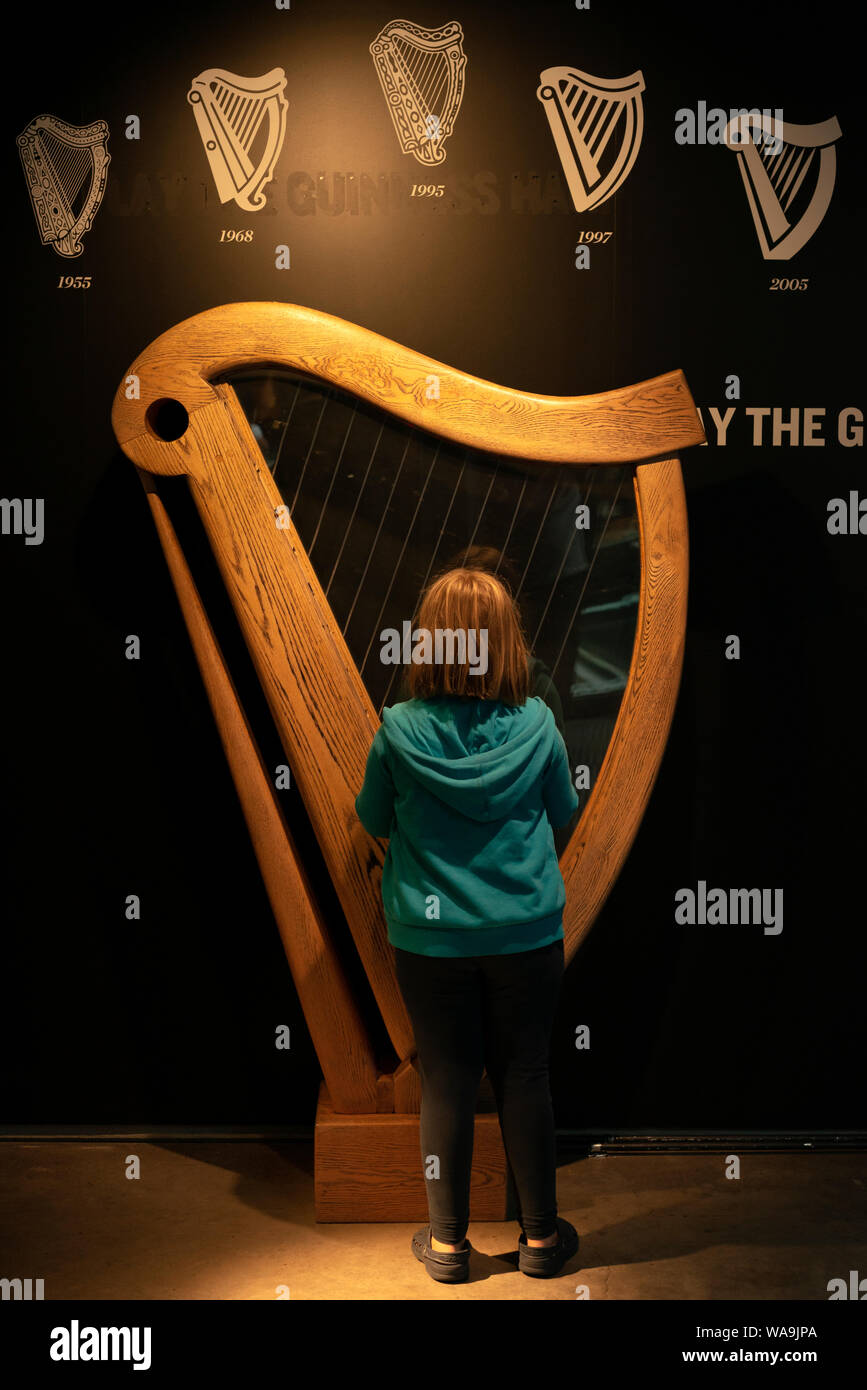 Ireland tourism young tourist girl playing on a Guinness Irish harp replica in the Guinness Storehouse and Museum, Dublin, Ireland Stock Photo