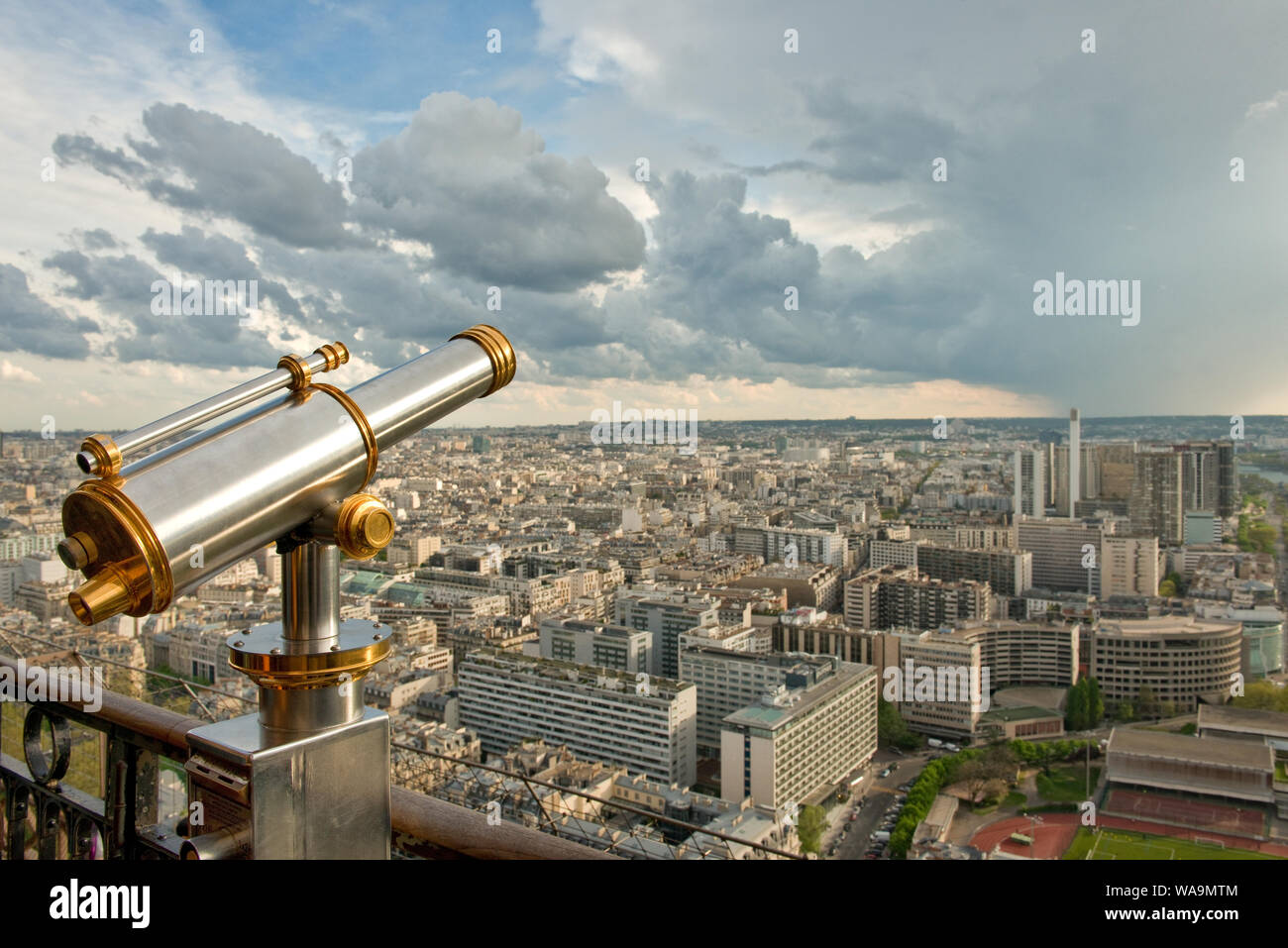 Coin-operated telescope on Eiffel Tower viewing platform. Looking south over city office buildings. With rain shower clouds. Paris, France Stock Photo