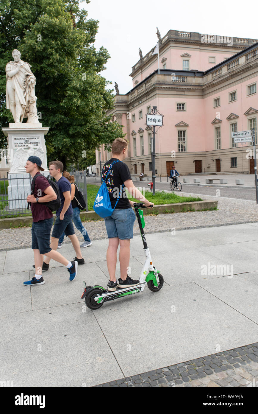 A young man on a Uber-owned LIME E-scooters on the sidewalk or pavement. E-Scooters have arrived recently in Berlin, Germany. Stock Photo