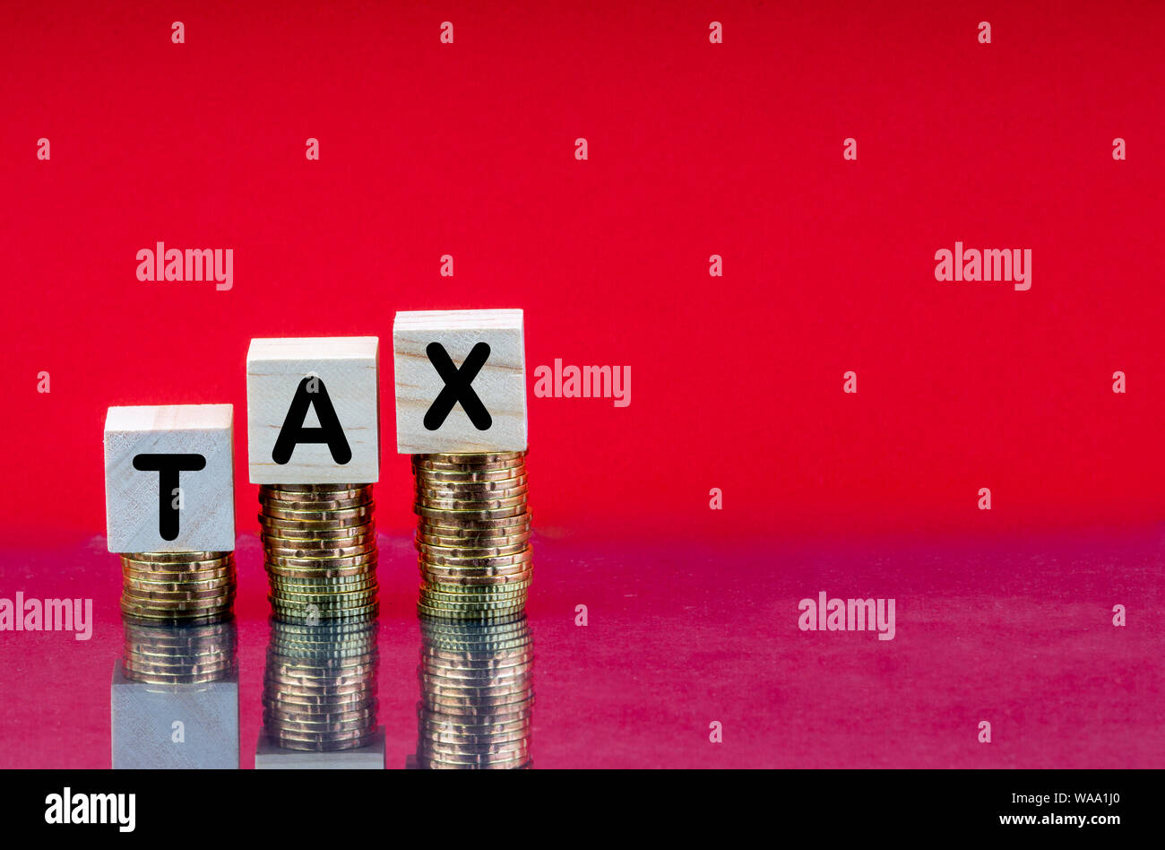 TAX Concept with wooden block on stacked coins and red background Stock Photo