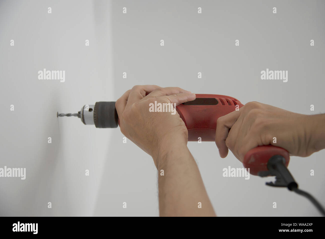 Man using hand drill device for installing home furniture at new white wall - people DIY home furniture installation concept Stock Photo
