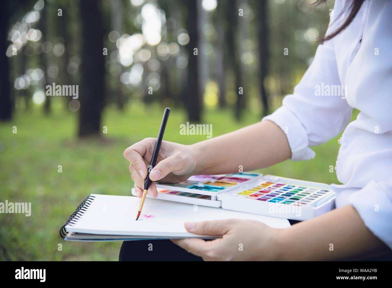 Relax woman painting water colour art work in green garden forest nature - people with creative art in nature stress reduction and meditation concept Stock Photo