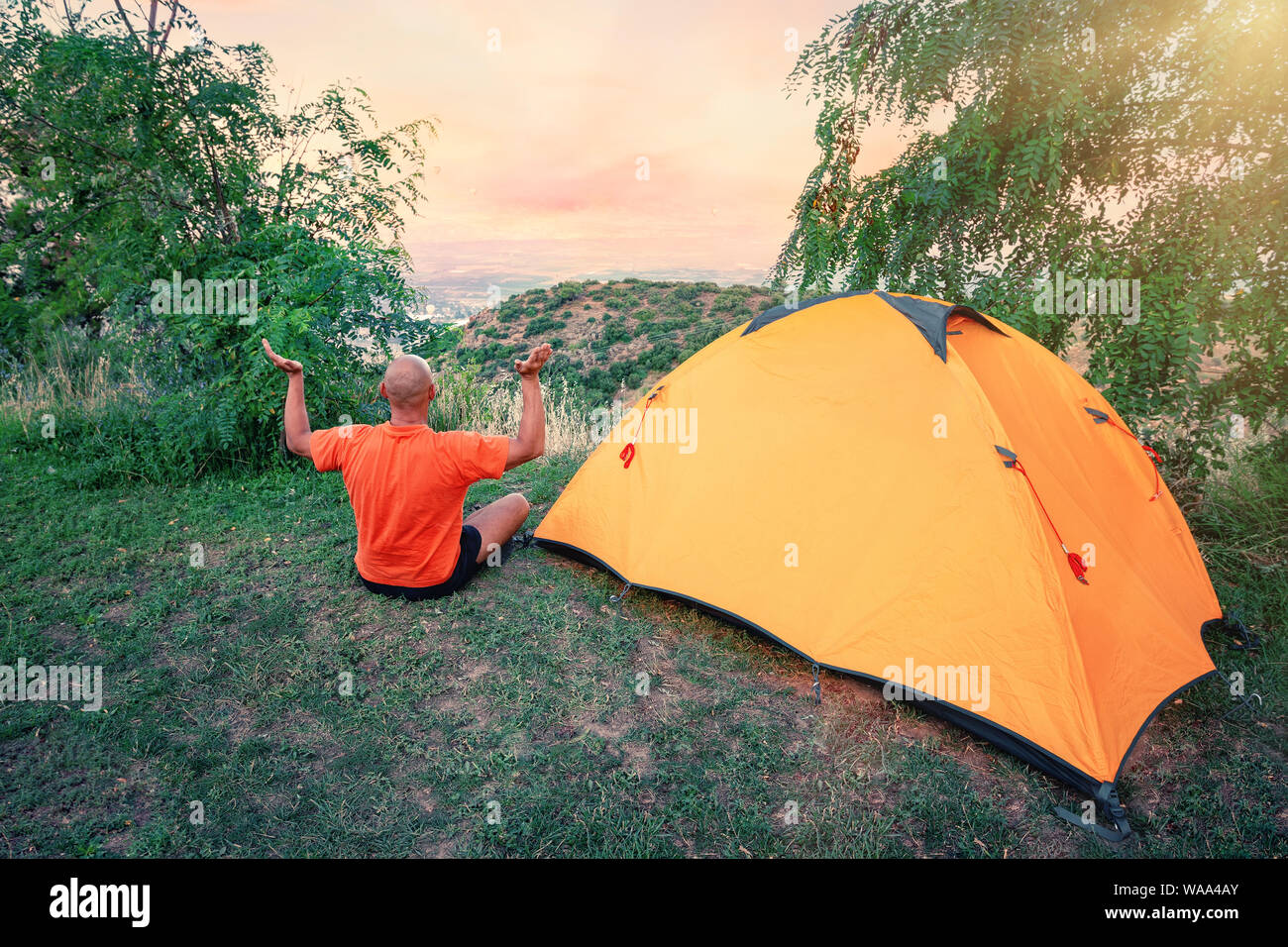 Man practices yoga near an orange tent on hill Stock Photo