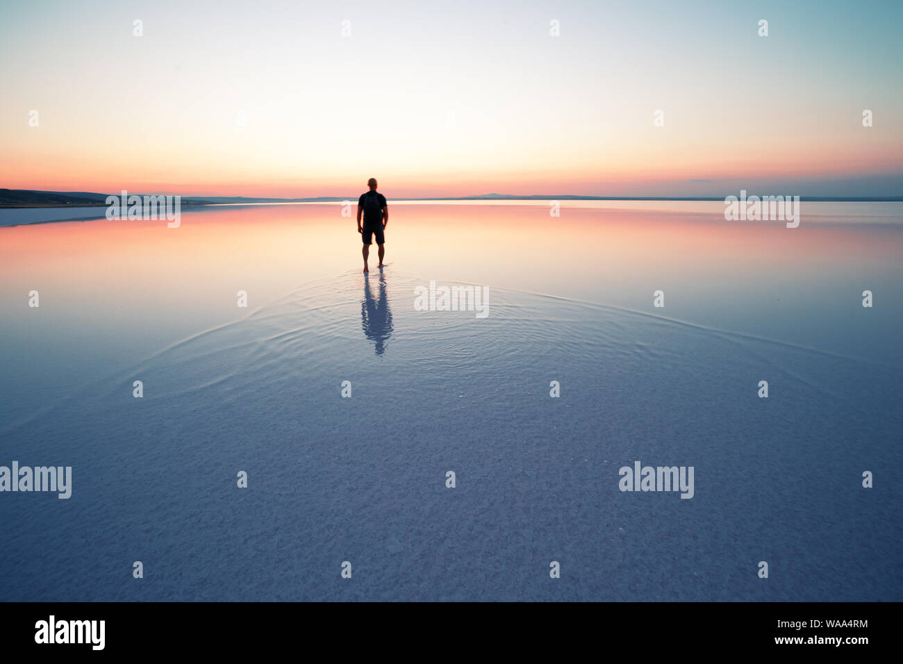Silhouette of man departing into sunset on smooth water of lake Stock Photo