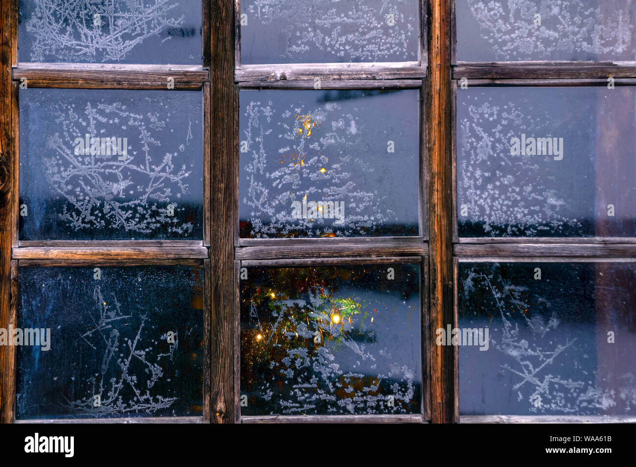 glowing christmas tree barely visible behind the frozen window glass with frosty patterns Stock Photo