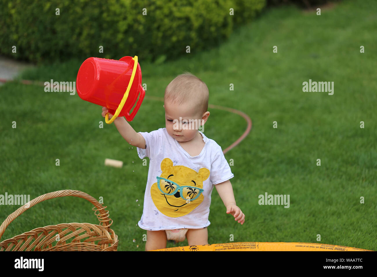 Baby beim Wasser plantschen mit rotem Kübel Stock Photo