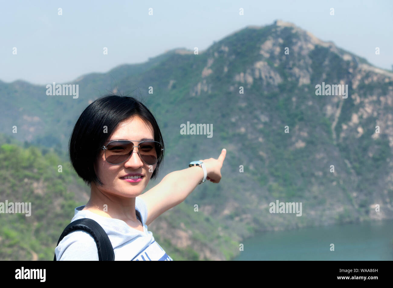 A Chinese Woman With Short Hair Wearing A Backpack Pointing At The
