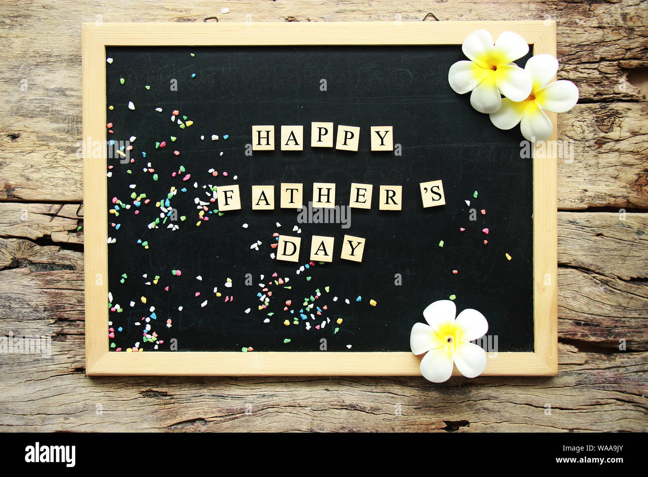 happy father's day word from wooden block place on black chalk board decorate with tropical flower on wooden background Stock Photo