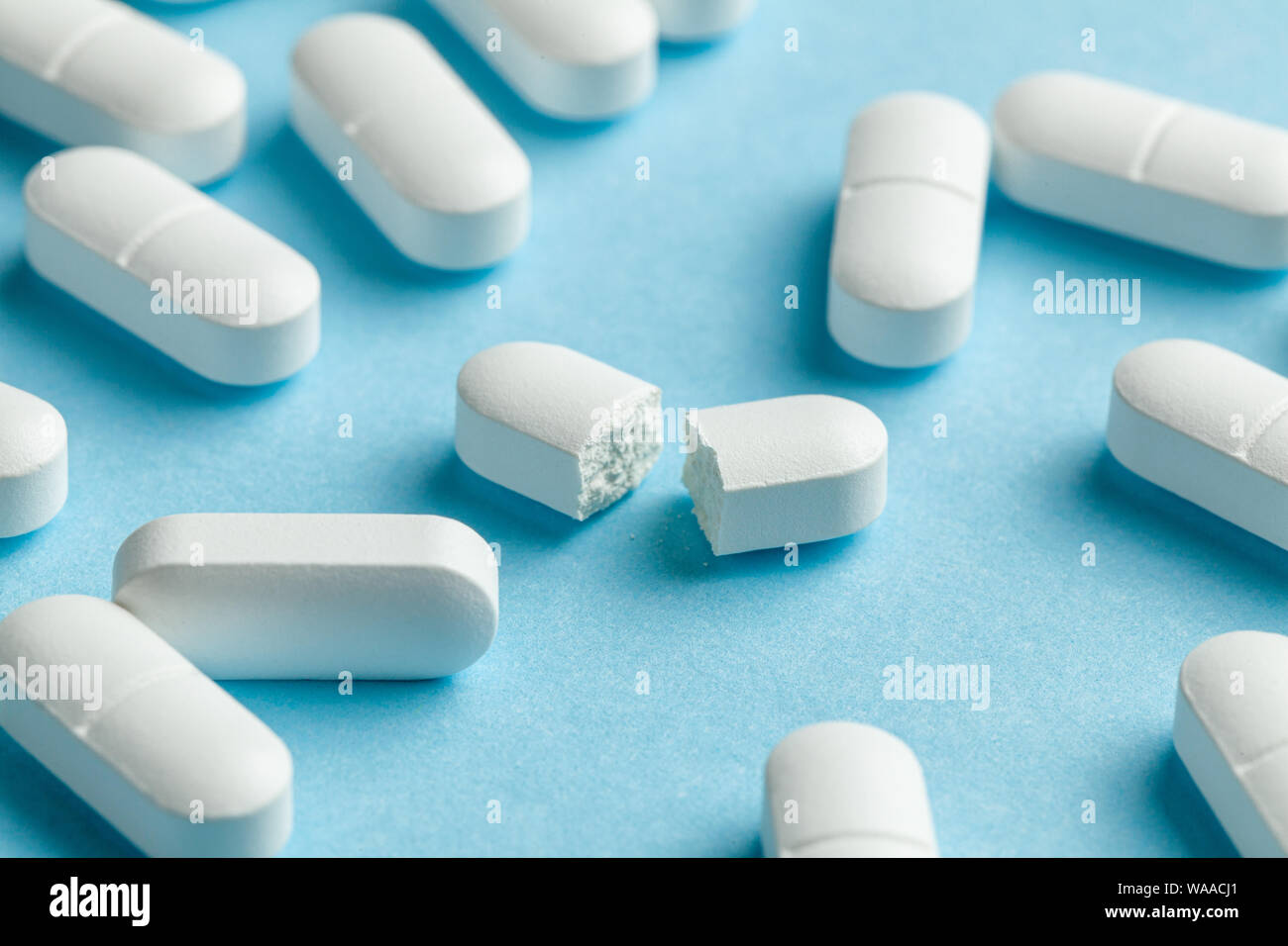 White Pills On Blue Background One Tablet Is Broken In Half Reducing The Dose Of The Medicine Stock Photo Alamy
