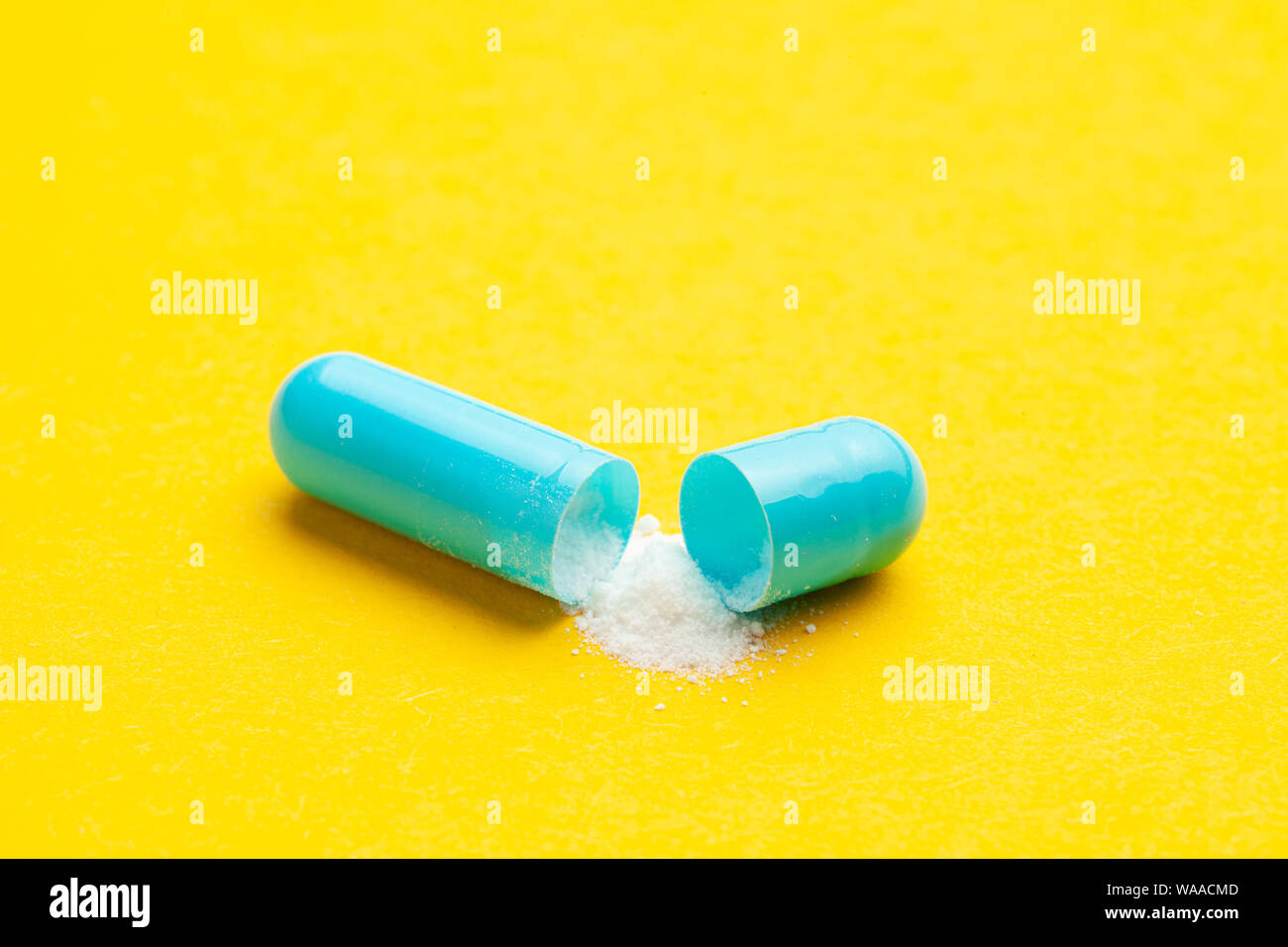 Blue tablets in capsules. One capsule is open. Yellow background Stock