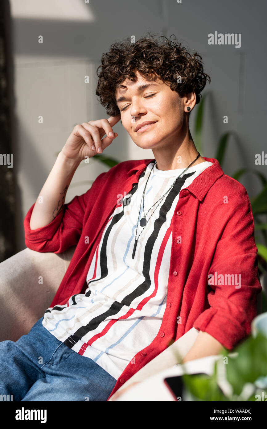 Young delighted woman in smart casual sitting in armchair after work Stock Photo