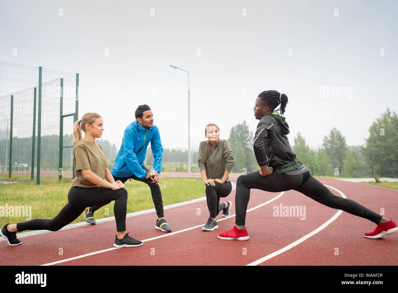 Four young friendly active people in sportswear exercising on racetracks Stock Photo