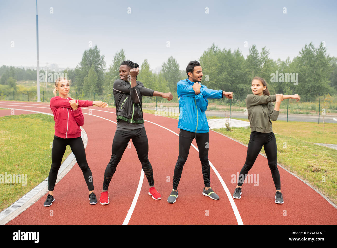Young men and women in activewear exercising on race tracks Stock Photo