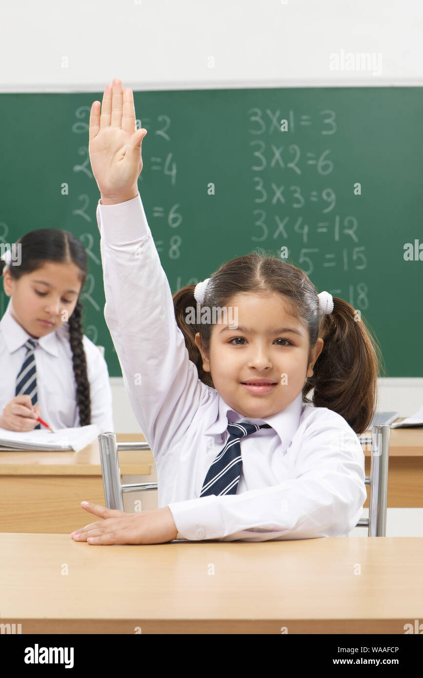 Schoolgirl raising hand in classroom Stock Photo