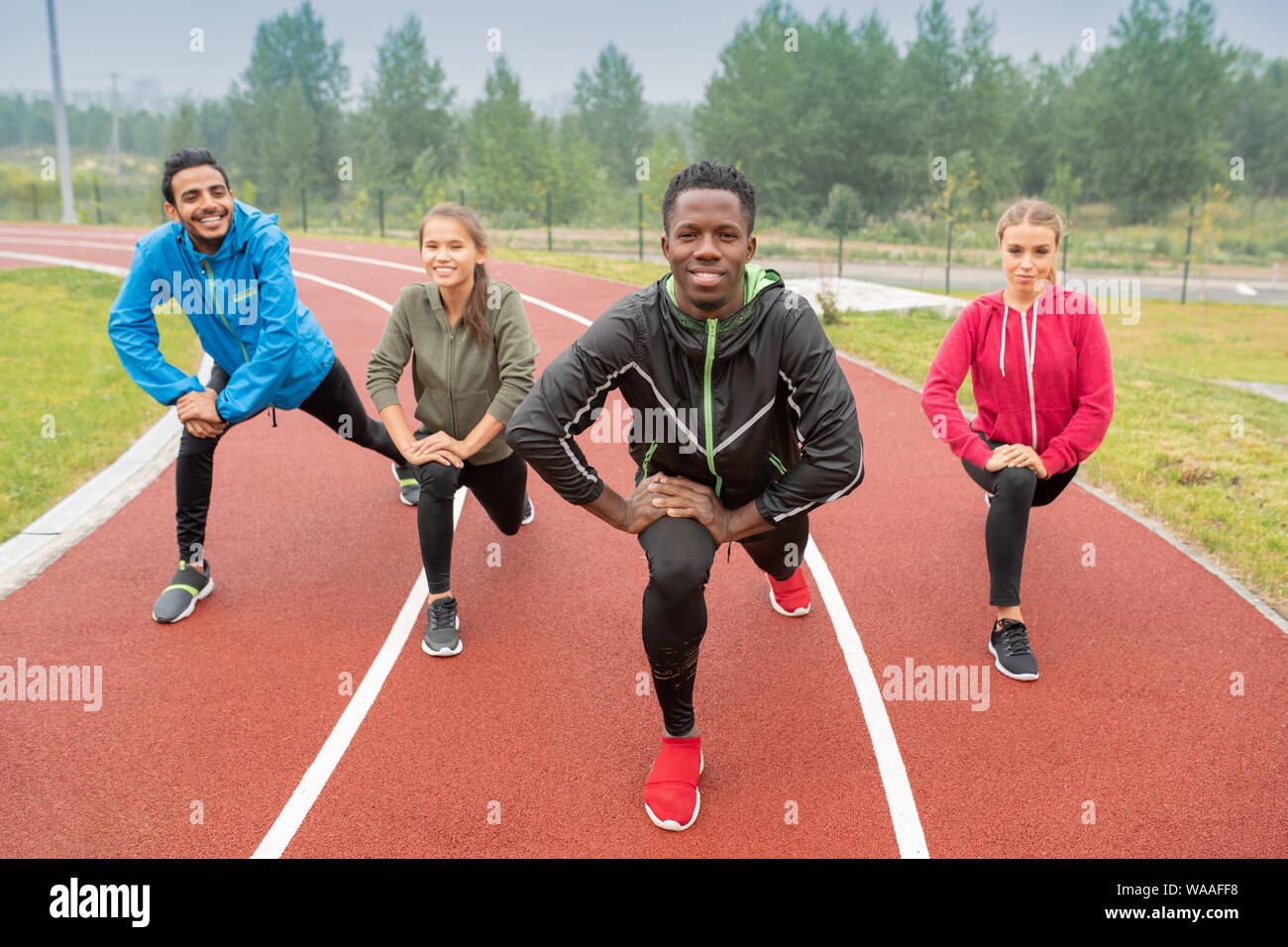 Healthy young intercultural friends in activewear exercising on race tracks Stock Photo